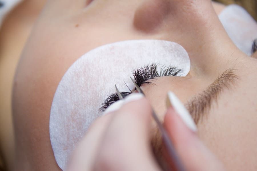 Primer plano de una técnica que utiliza pinzas para aplicar extensiones de pestañas individuales en el ojo de una clienta.