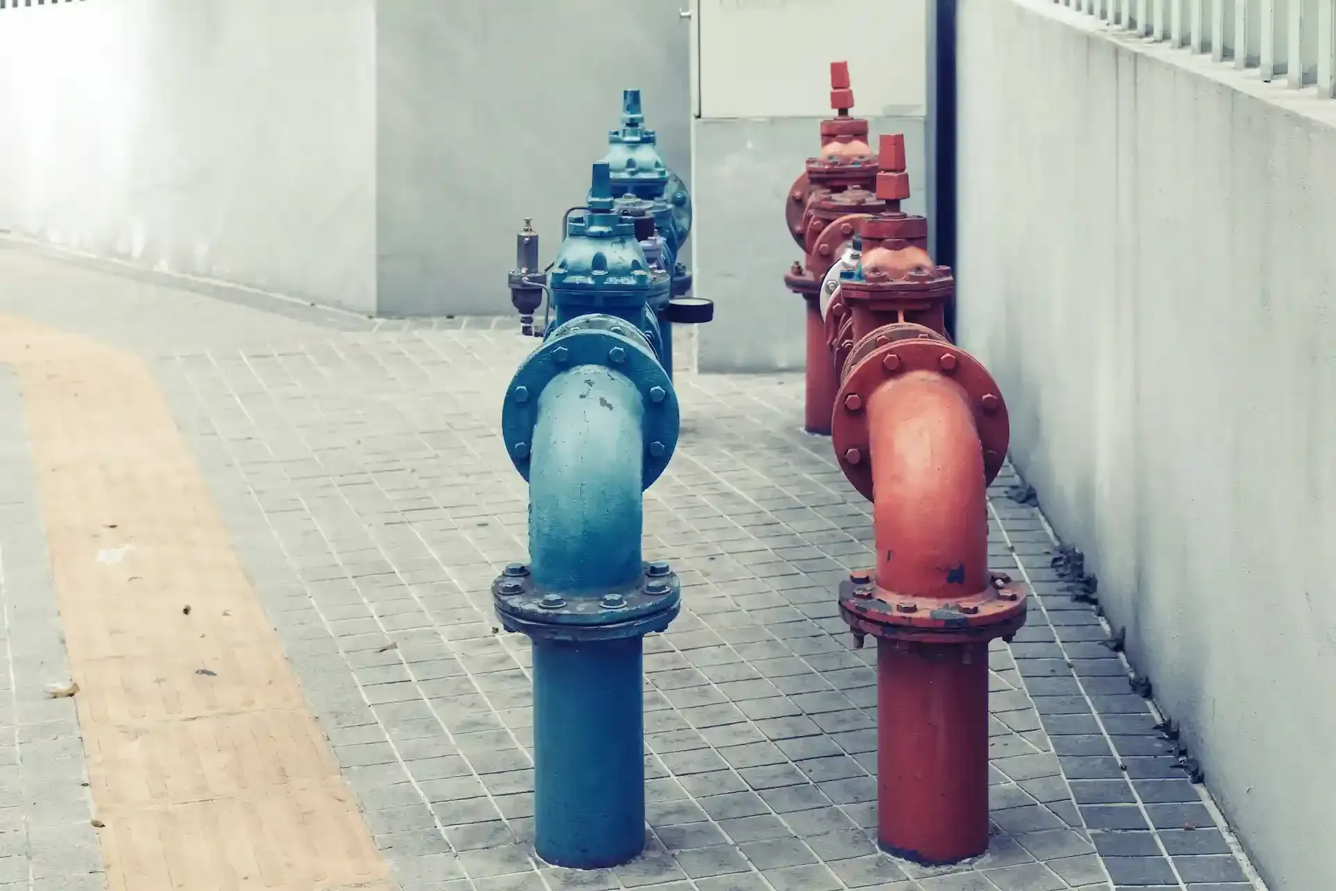 Tubos azules y rojos con válvulas alineadas sobre una superficie de ladrillo y hormigón.