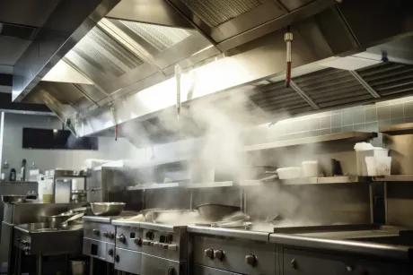 Cocina comercial con vapor saliendo de las estufas debajo de una campana extractora de acero inoxidable.