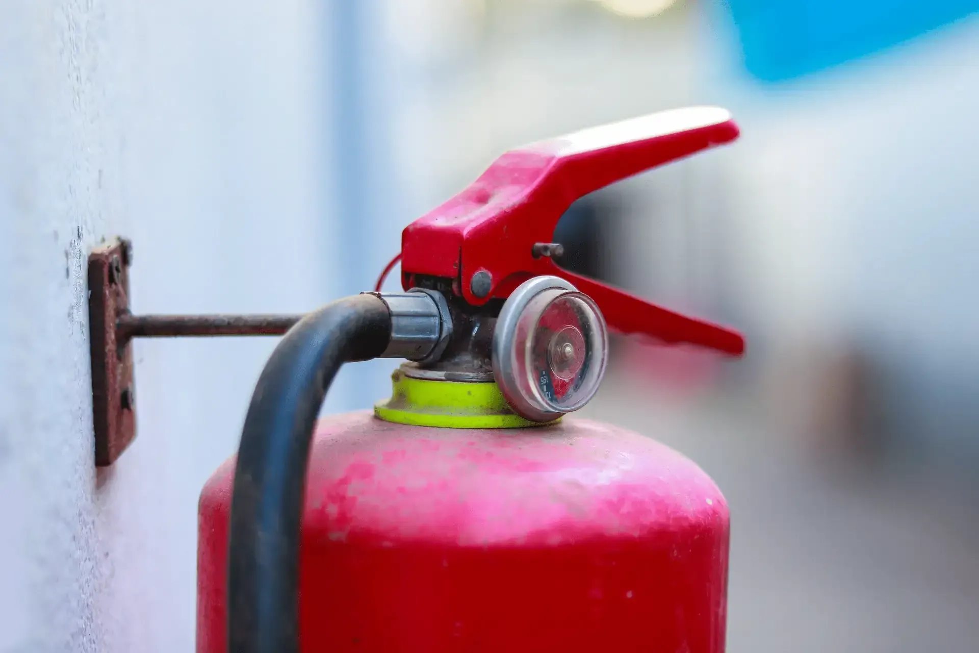 Extintor rojo montado en una pared blanca, con manómetro.