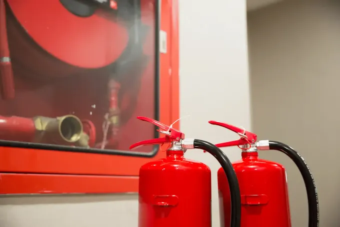Extintores rojos y un armario con mangueras contra incendios en una pared.
