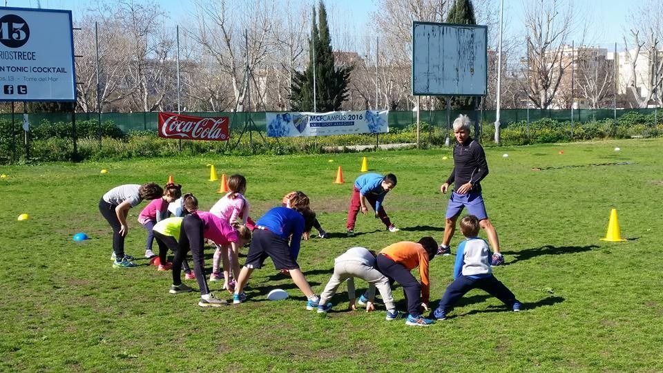 Un grupo de niños está jugando en un campo con un cartel de Coca Cola en el fondo.