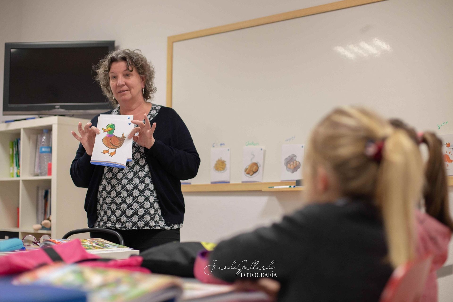 Una mujer está parada frente a un salón de clases sosteniendo una foto de un pato.