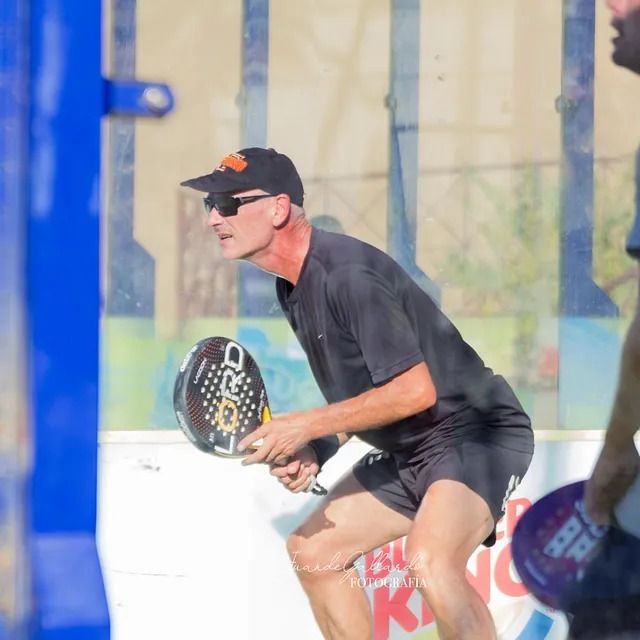 Un hombre con una camisa negra sostiene una raqueta de pádel que tiene escrito O'Neill.