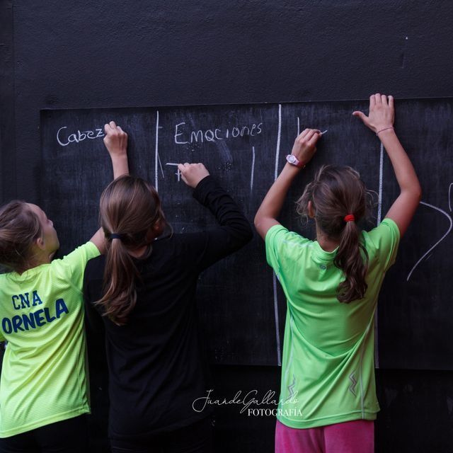 Tres niños están parados frente a una pizarra con la palabra emociones escrita en ella.