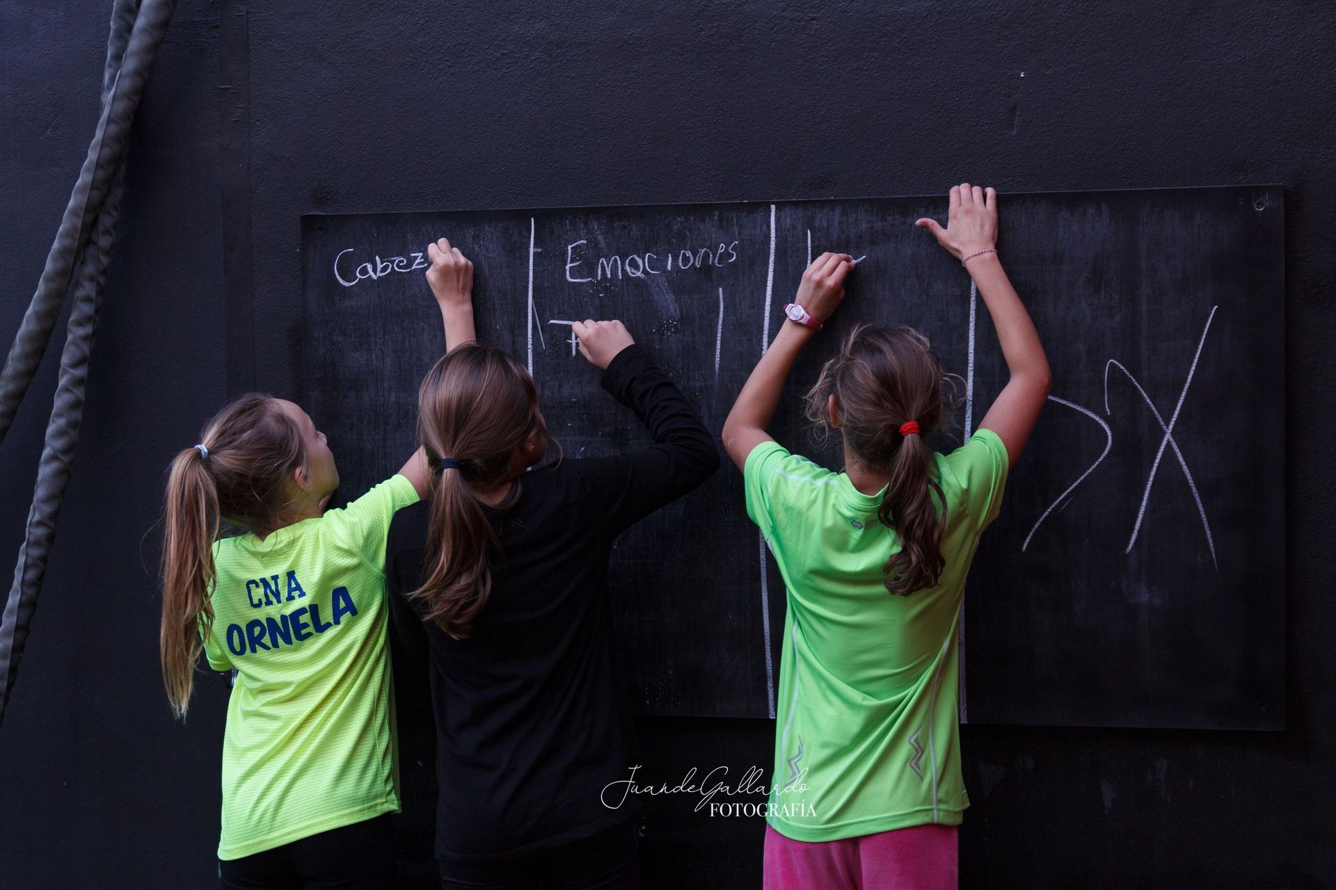 Tres chicas con camisetas verde neón escriben en una pizarra.