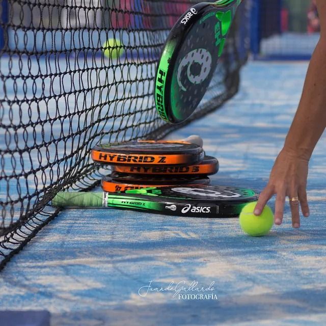 Una persona alcanza una pelota de tenis frente a una pila de raquetas híbridas 1.