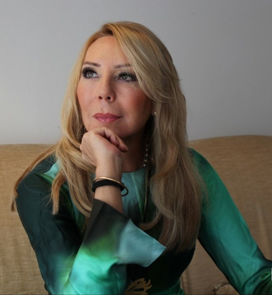 Mujer rubia con vestido verde, mano en la barbilla, mirada pensativa.