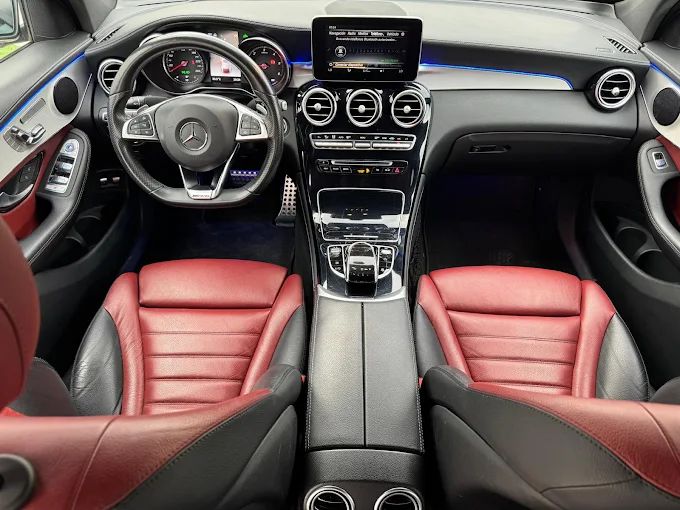 Vista interior del habitáculo de un coche moderno con salpicadero negro, volante y asientos deportivos de cuero rojo y negro.