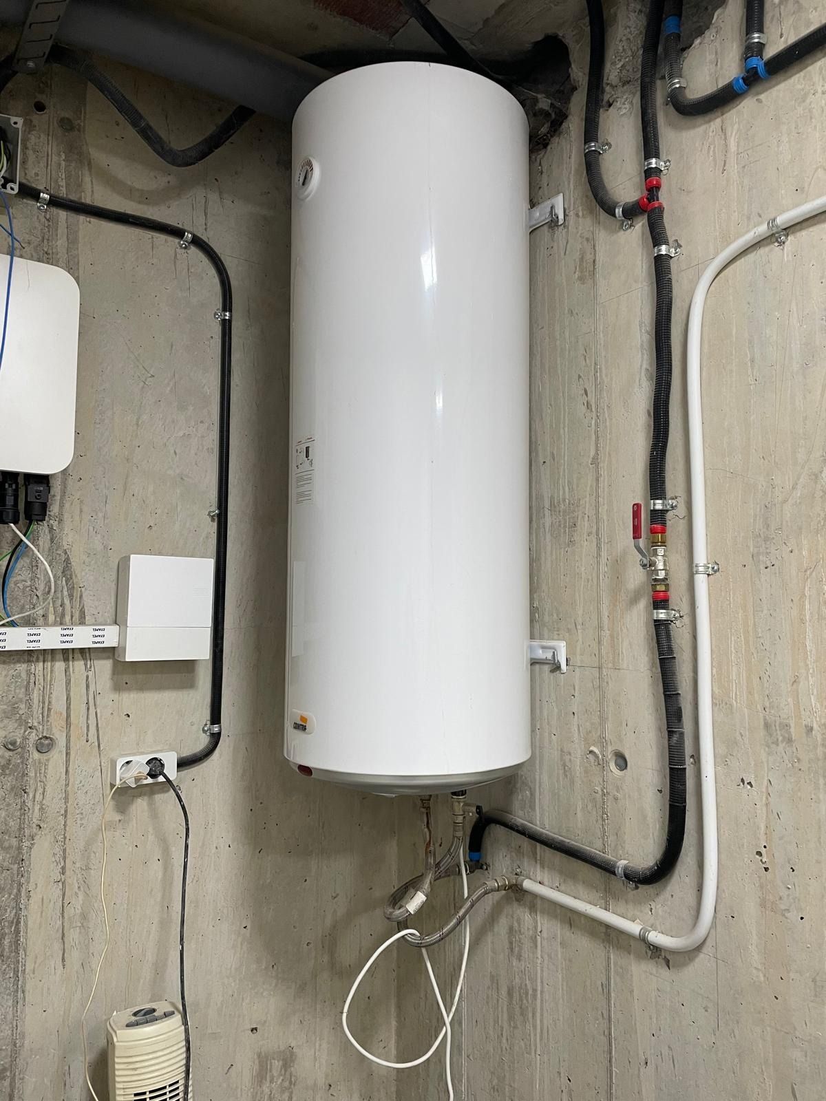Tanque de calentador de agua blanco montado sobre una pared de hormigón con tuberías y cableado 