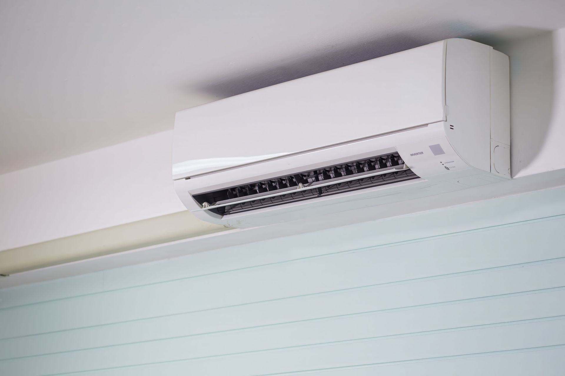 Aire acondicionado blanco montado en la pared, instalado cerca del techo en el interior.