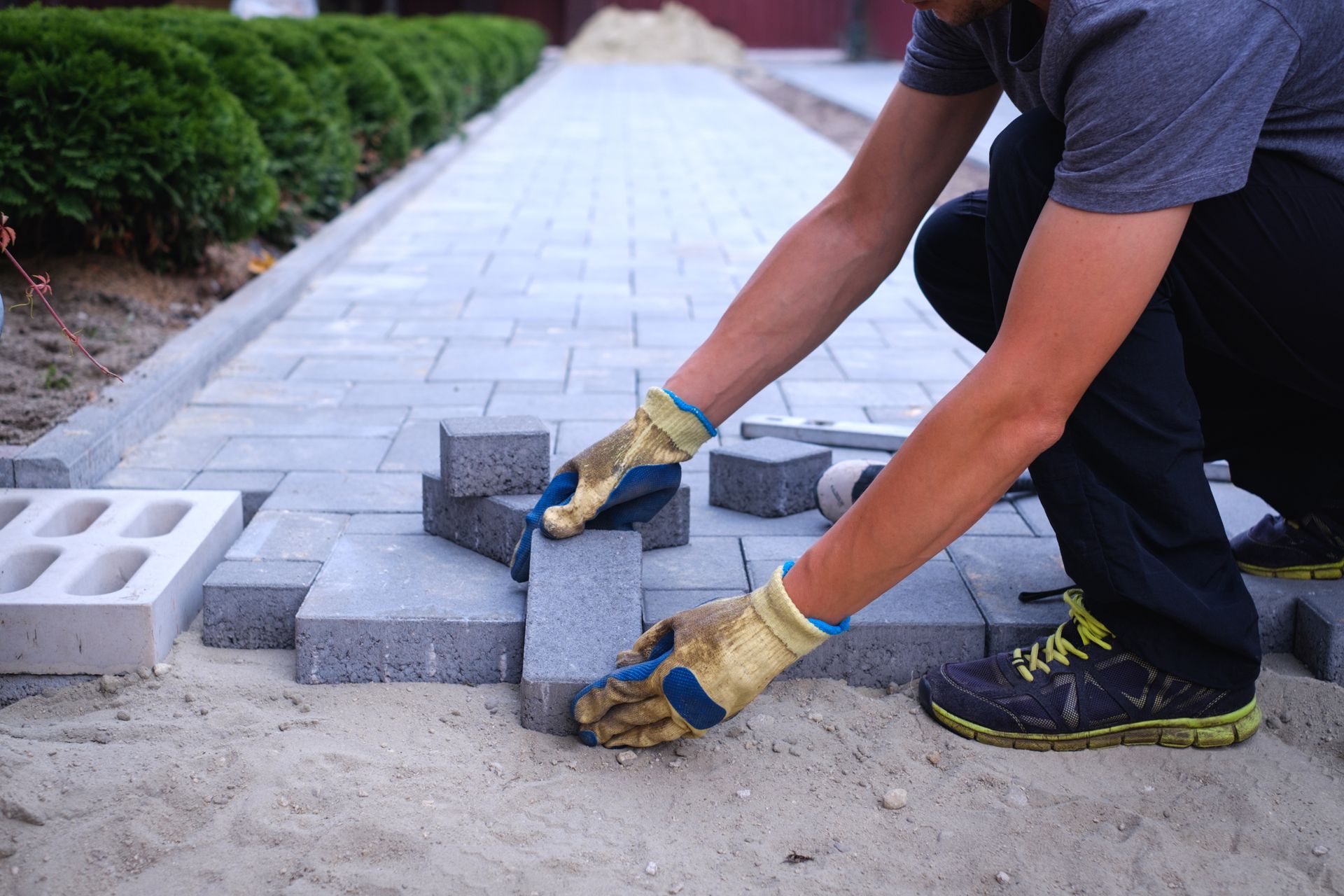 Une personne pose des pavés sur un sol sablonneux. Travaux de construction d'une allée.