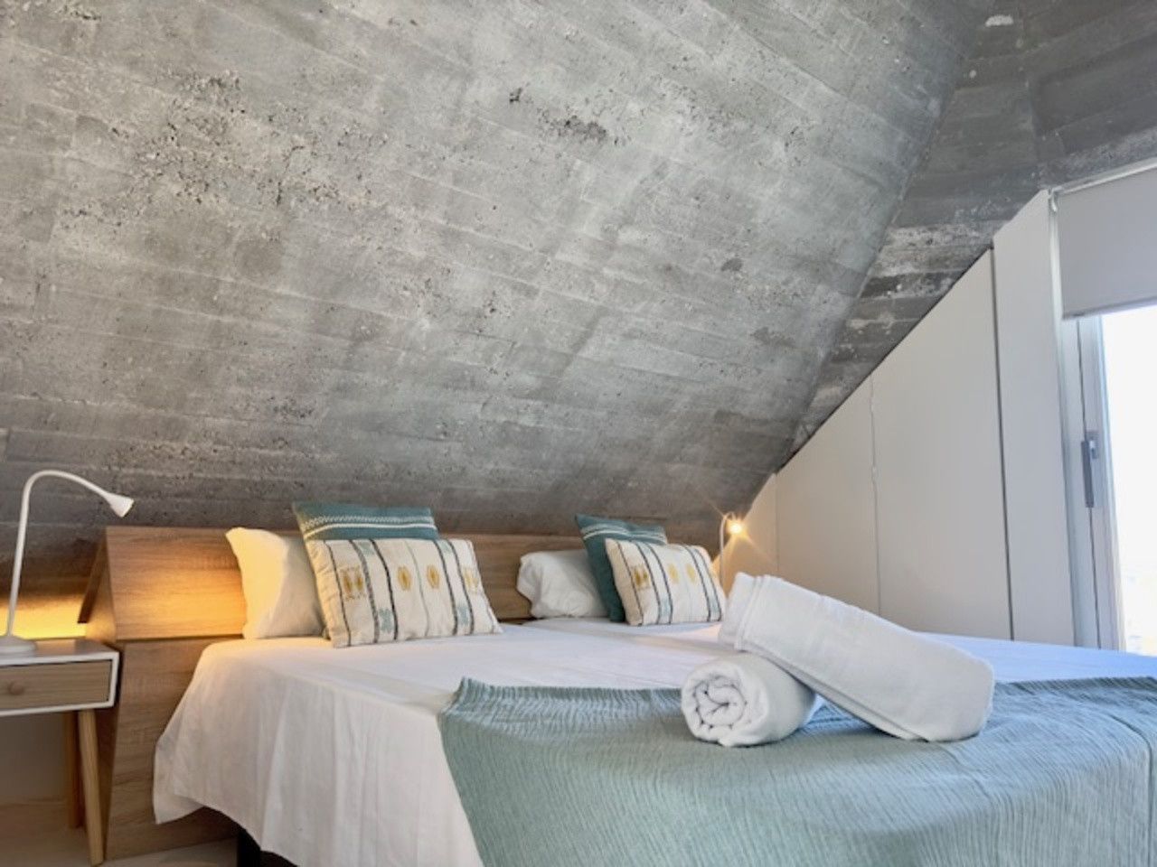 Un dormitorio con dos camas y una pared de hormigón.