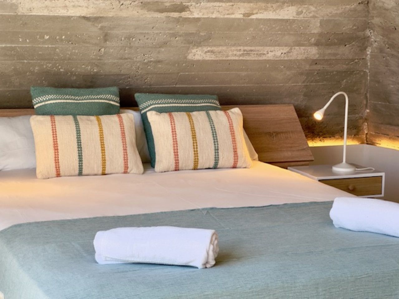 Un dormitorio con una cama, almohadas, una mesita de noche y una lámpara.