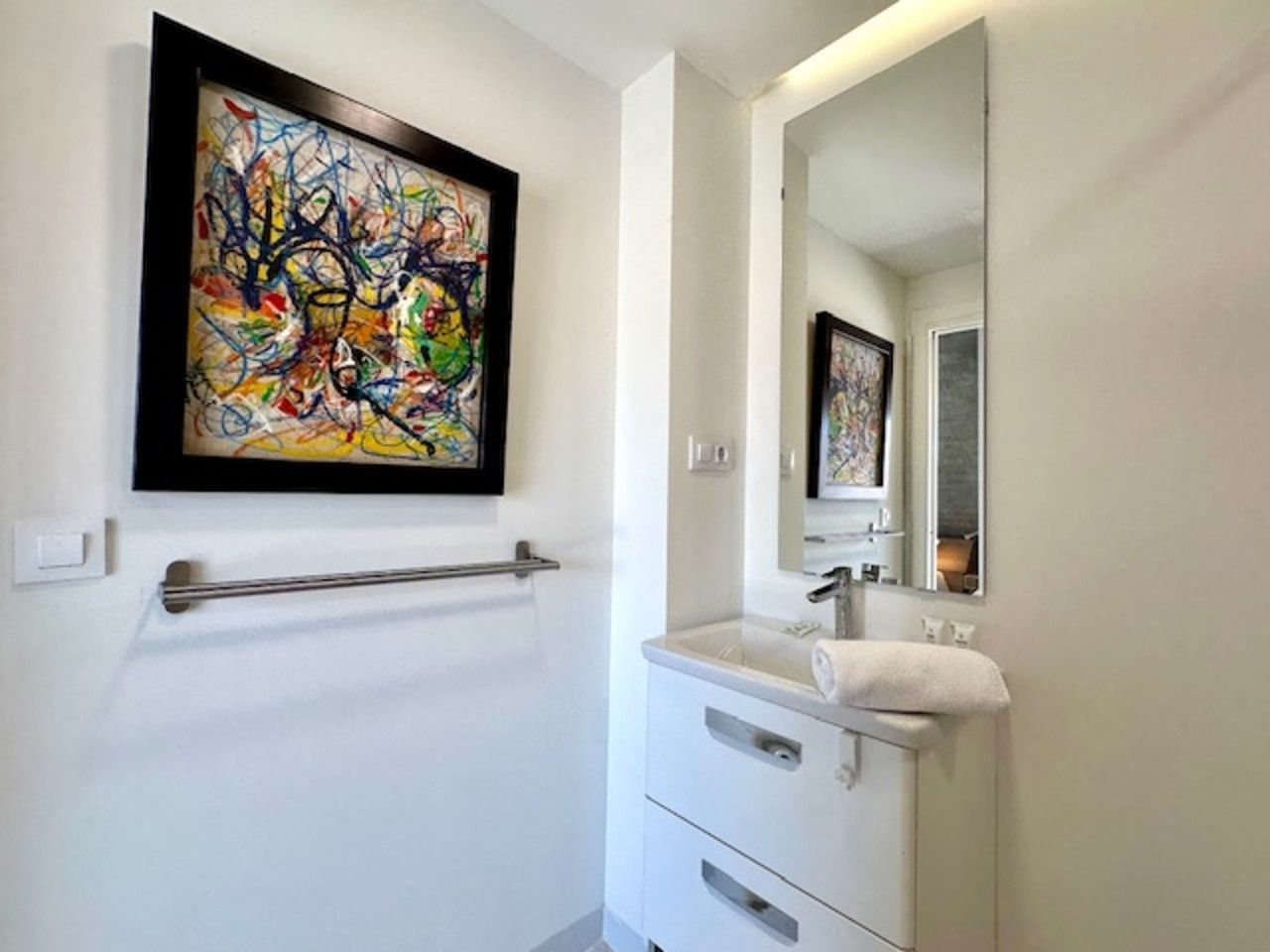 Un baño con lavabo, espejo y cuadro en la pared.