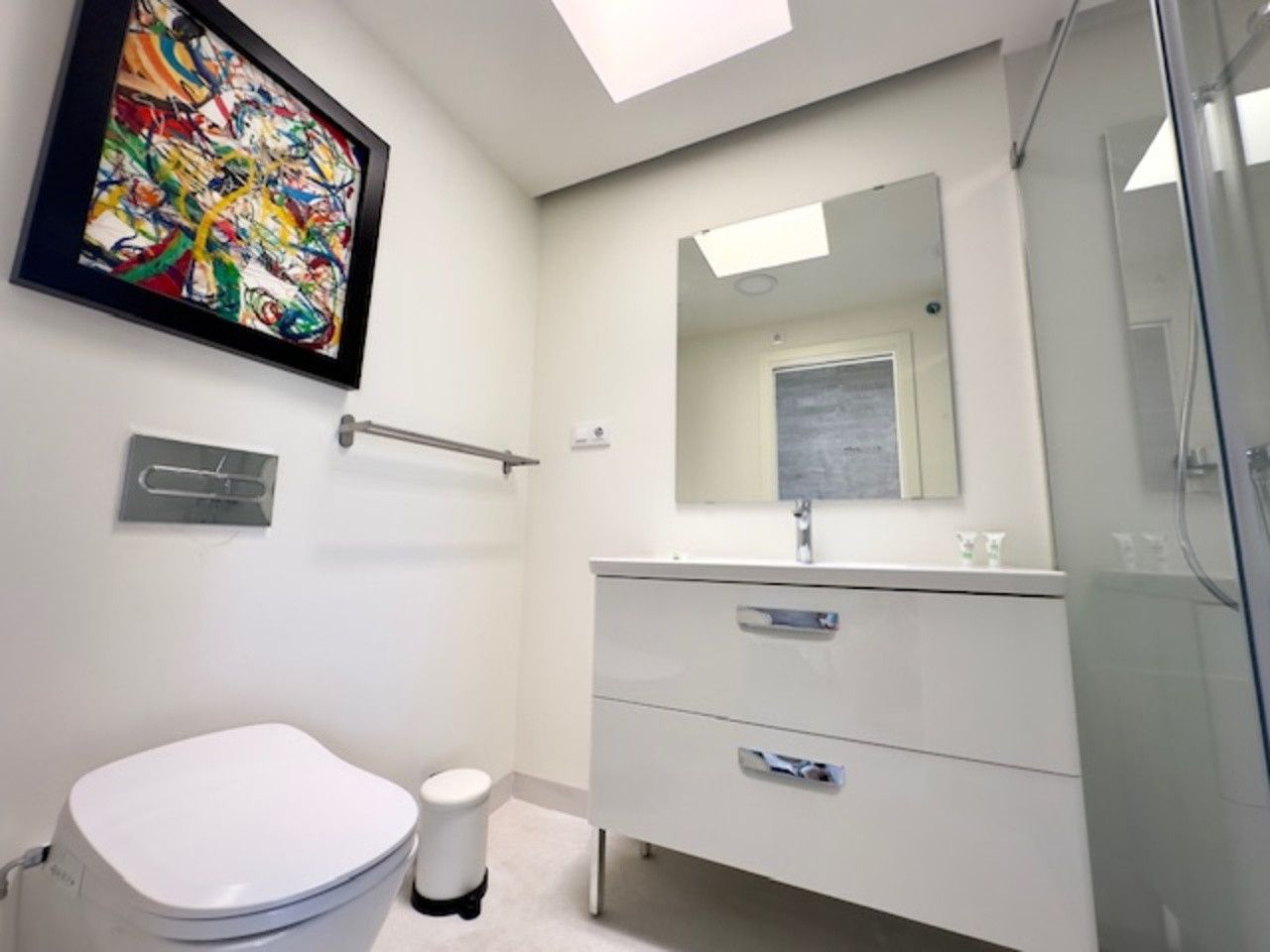 Un baño con inodoro, lavabo, espejo y cuadro en la pared.