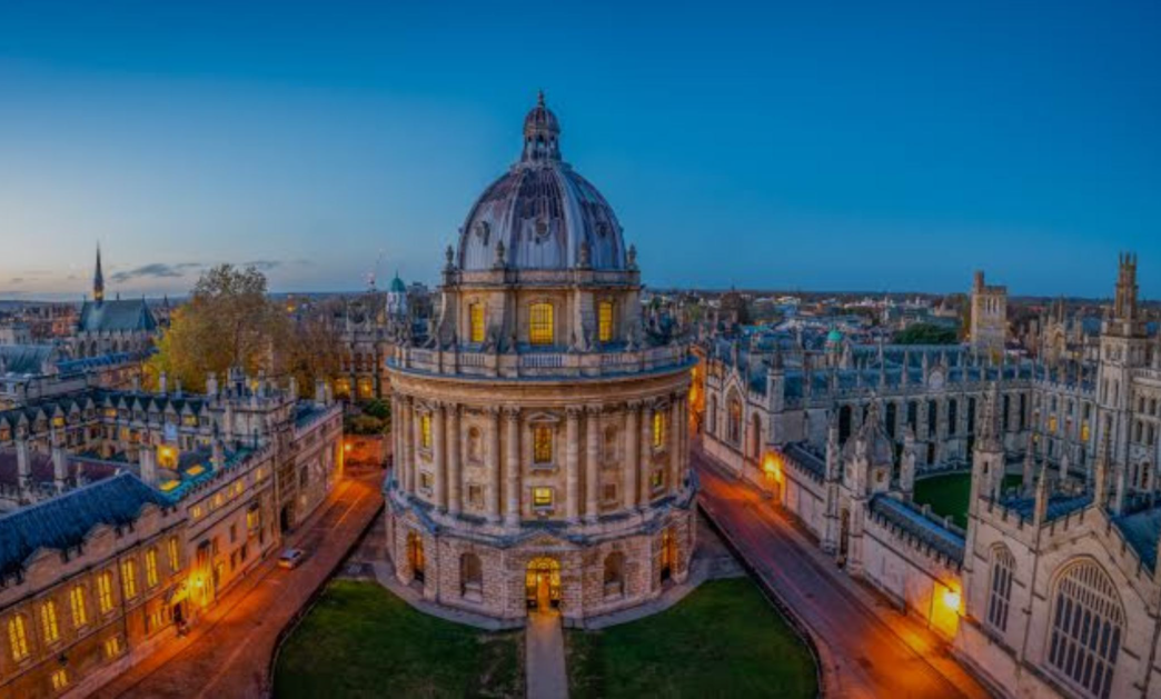 Image shows University of Oxford buildings lit up at dusk