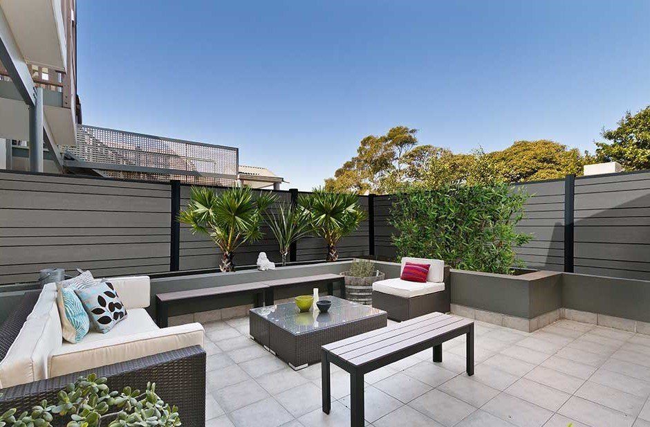 Terrasse avec mobilier de jardin, murs gris, verdure et ciel d'un bleu éclatant.