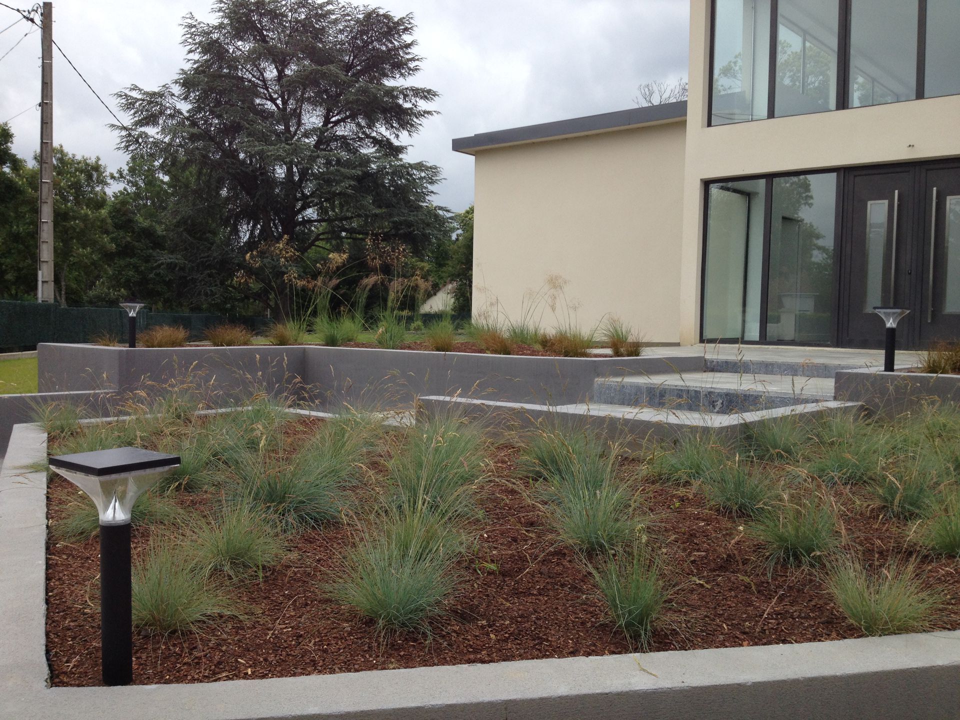 Aménagement paysager moderne avec jardinières étagées et gazon ornemental, éclairé par des lampes solaires.