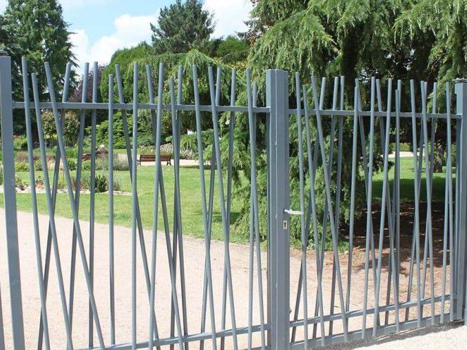 Clôture métallique grise à barreaux verticaux courbés devant un parc.