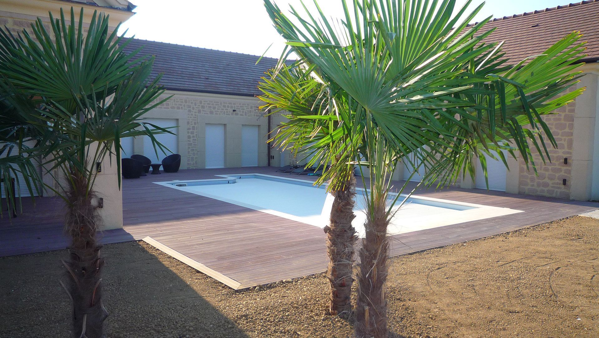 Des palmiers encadrent une piscine et une terrasse devant un bâtiment en briques claires.