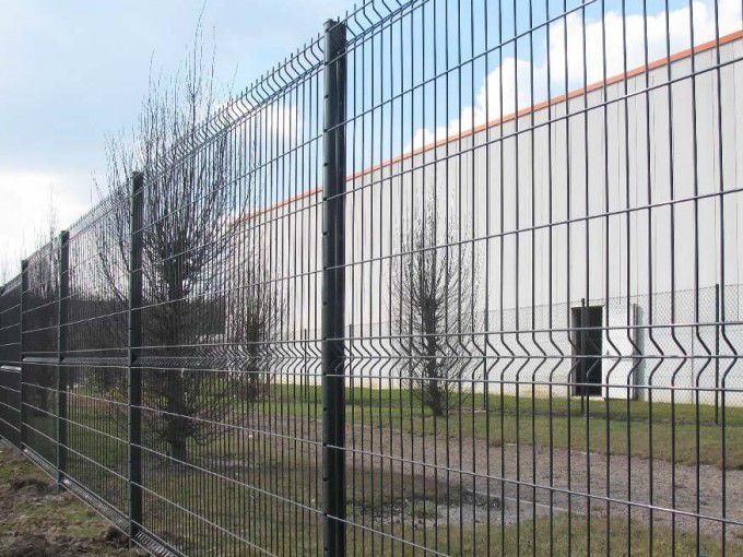 Clôture en grillage vert devant un bâtiment blanc avec des arbres dénudés.