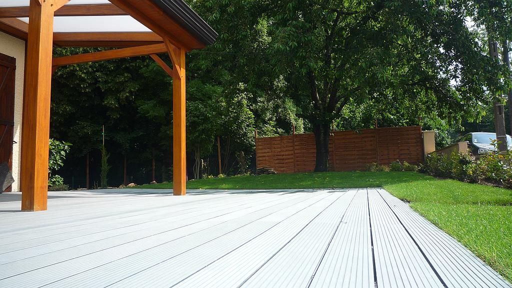 Terrasse en bois avec pergola, gazon et arbres.