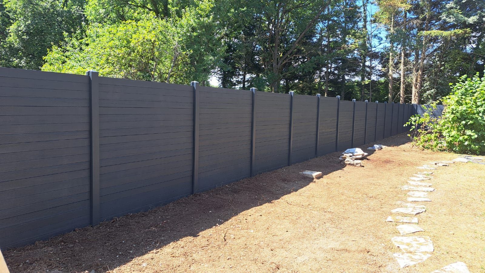 Clôture d'intimité gris foncé dans une cour arrière, sol en gravier, arbres en arrière-plan.
