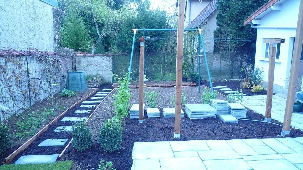 Cour arrière avec pas japonais, balançoire et aménagement paysager, comprenant une terrasse et un mur de pierre.