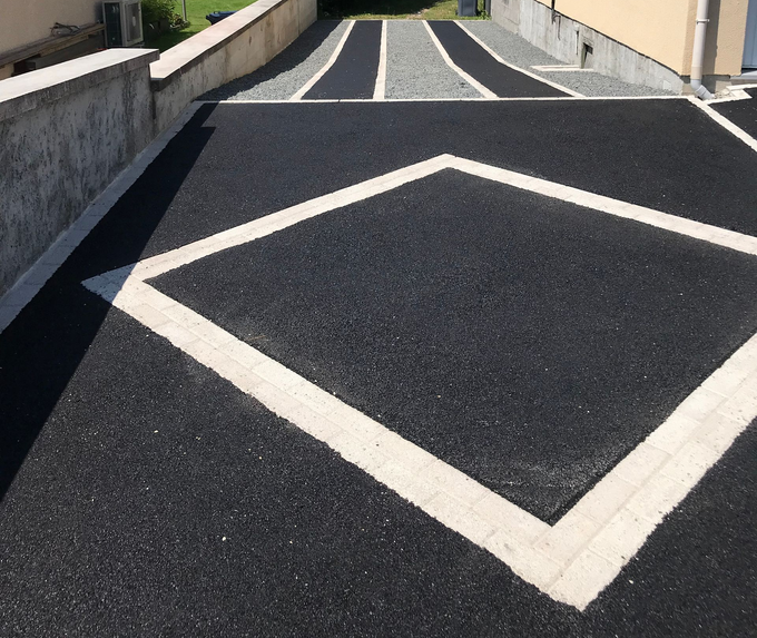 Allée pavée de noir avec un motif en losanges clairs et des bandes de gravier.