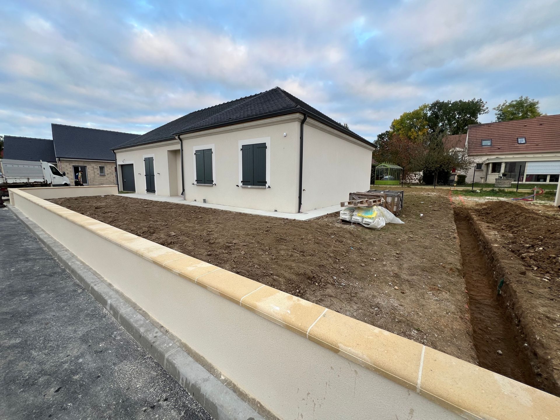 Maison neuve beige avec volets noirs, toit et cour avant en construction.