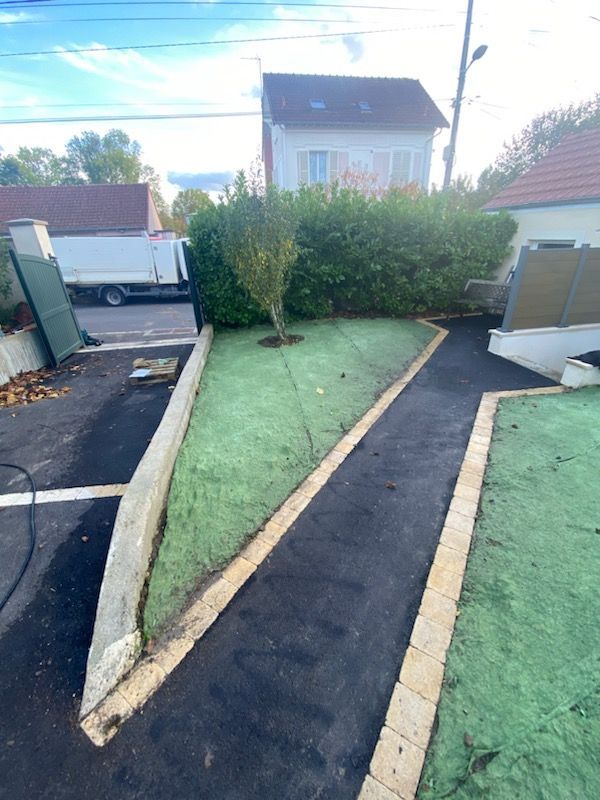 Allée asphaltée menant à une cour gazonnée bordée de briques. Un arbre et une haie sont également présents.