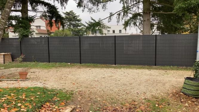 Clôture d'intimité gris foncé dans la cour arrière, avec un sol en gravier et des arbres en arrière-plan.