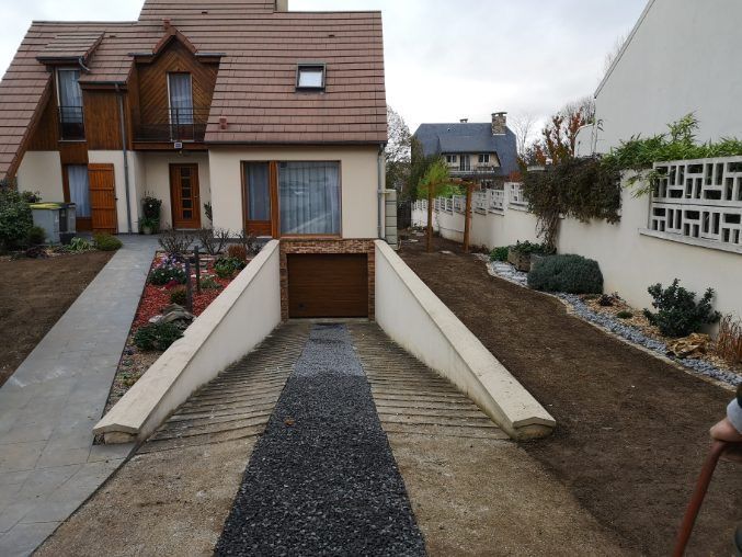 Maison avec allée menant à un garage. Murs en béton et chemin de gravier devant la porte de garage marron.