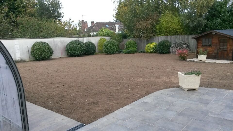 Une pelouse nouvellement semée avec des arbustes, un abri de jardin et une terrasse dans un jardin.