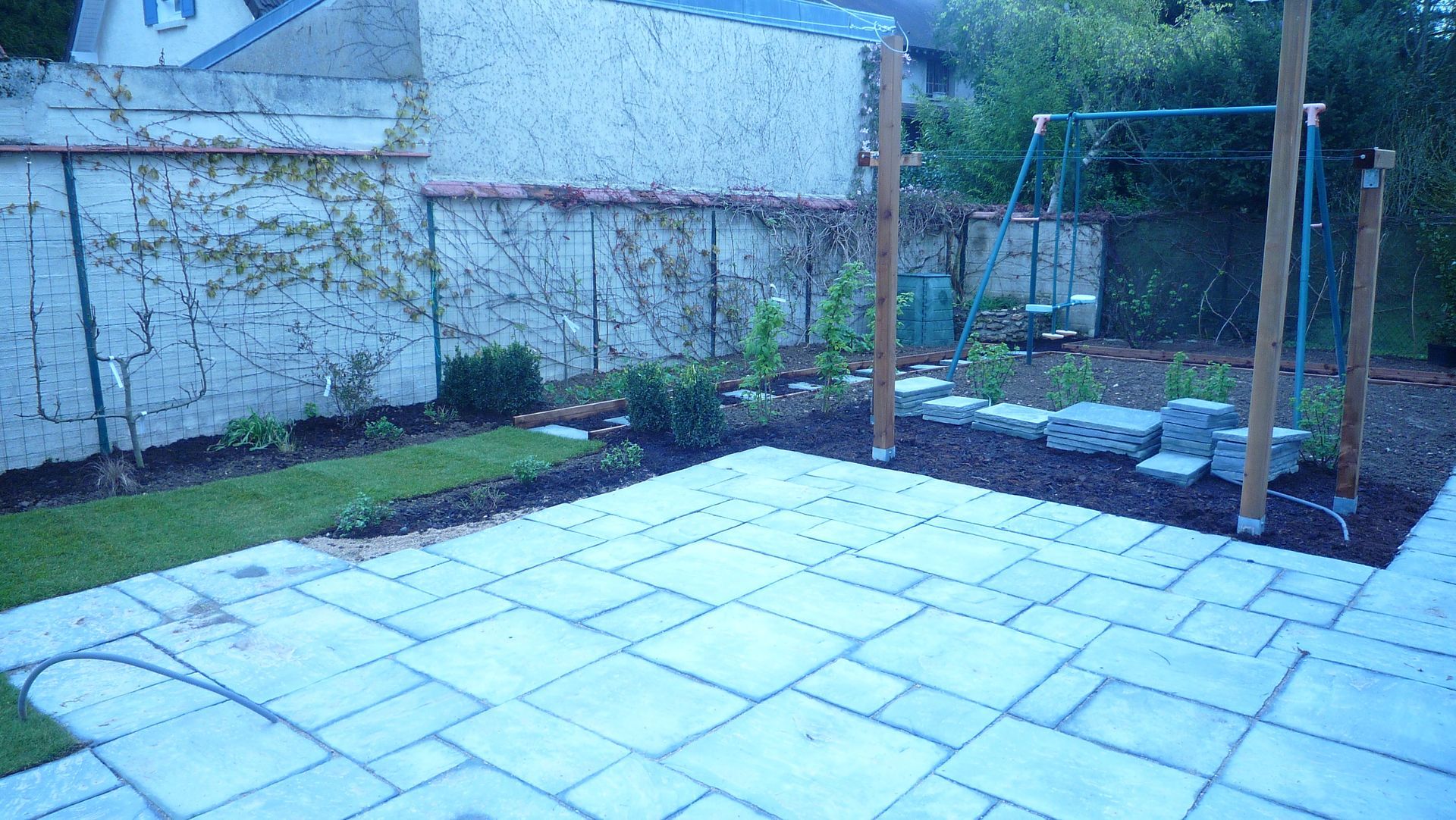 Terrasse avec dalles de pierre, verdure et balançoire dans un jardin.