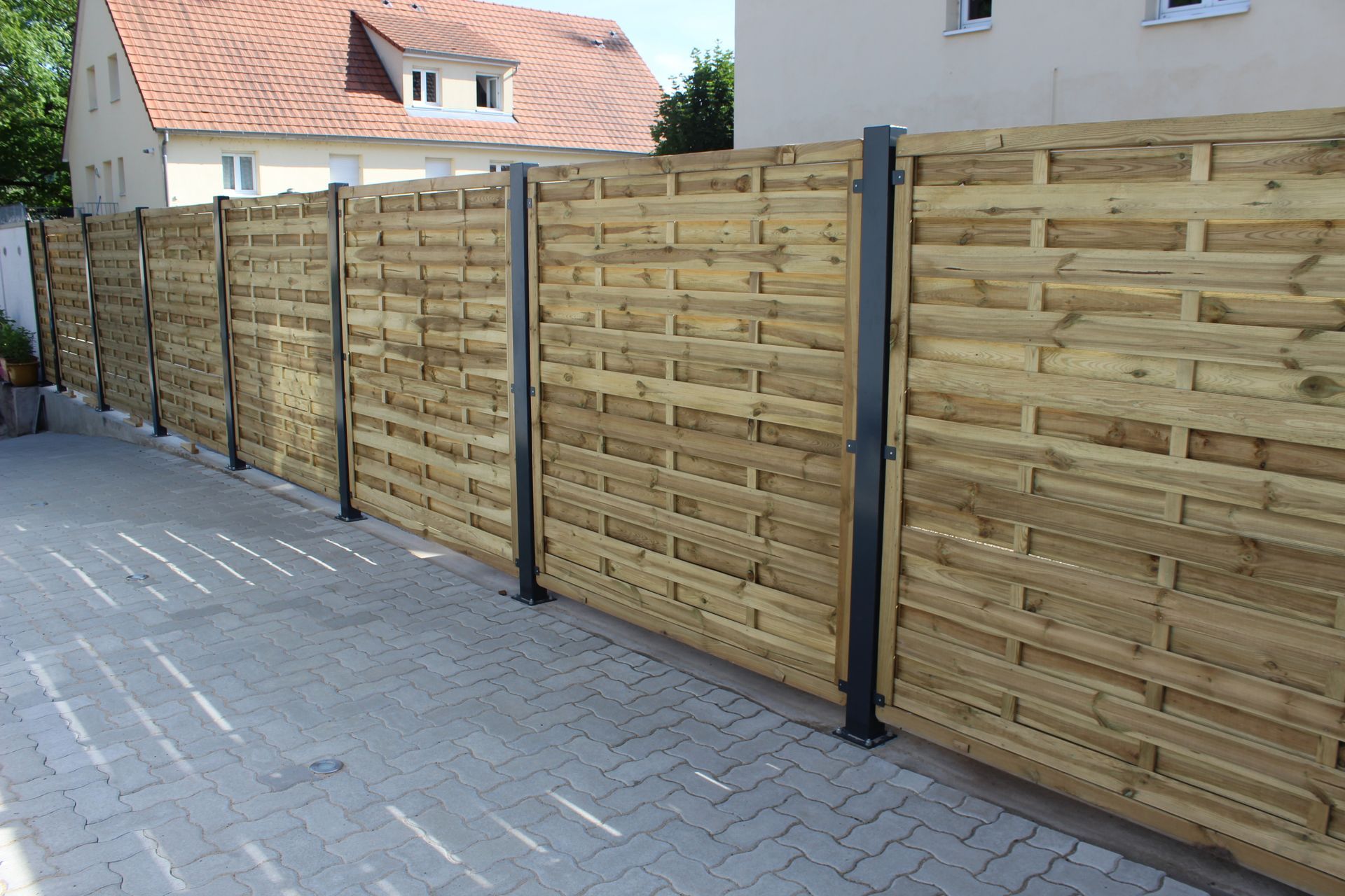 Clôture en bois avec poteaux en métal foncé, préservant l'intimité d'une maison sur une terrasse en briques.