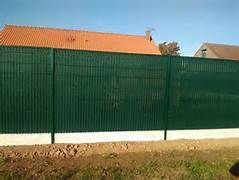 Clôture en tôle ondulée verte devant une maison au toit orange.