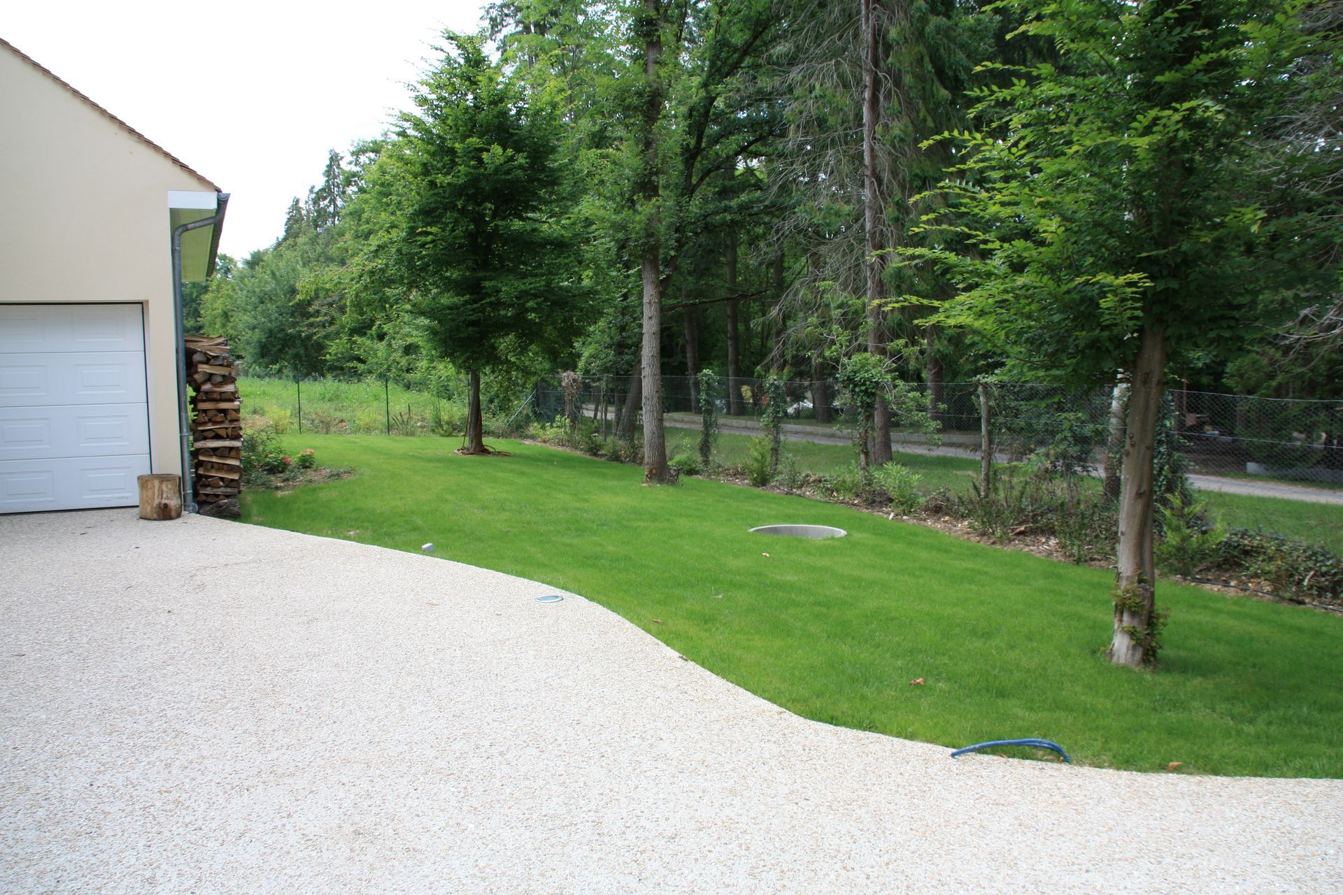 Allée de gravier incurvée menant à une pelouse arborée, près d'un bâtiment avec un garage.
