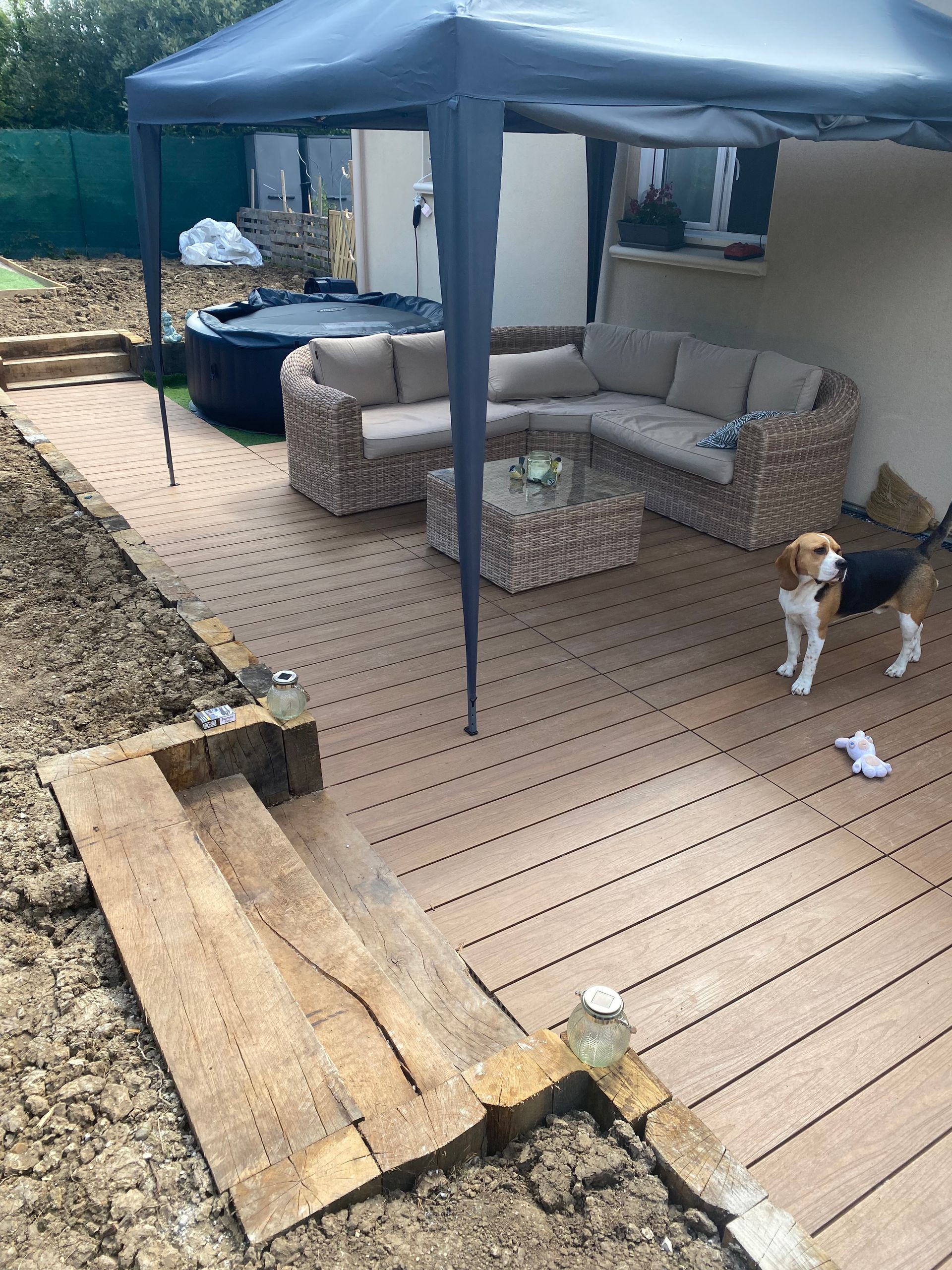 Terrasse beige avec canapé d'angle, jacuzzi, chien et auvent.