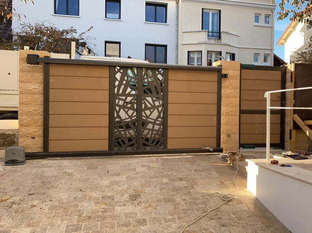 Portail marron et gris avec panneau central décoratif, colonnes en pierre beige et allée d'accès couleur sable.