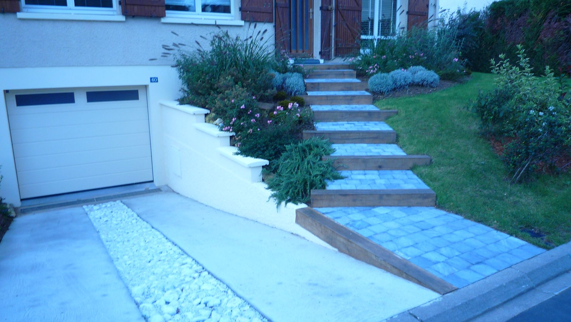 Une maison avec garage, escalier et aménagement paysager. L'escalier, entouré de plantes, mène à la porte d'entrée.