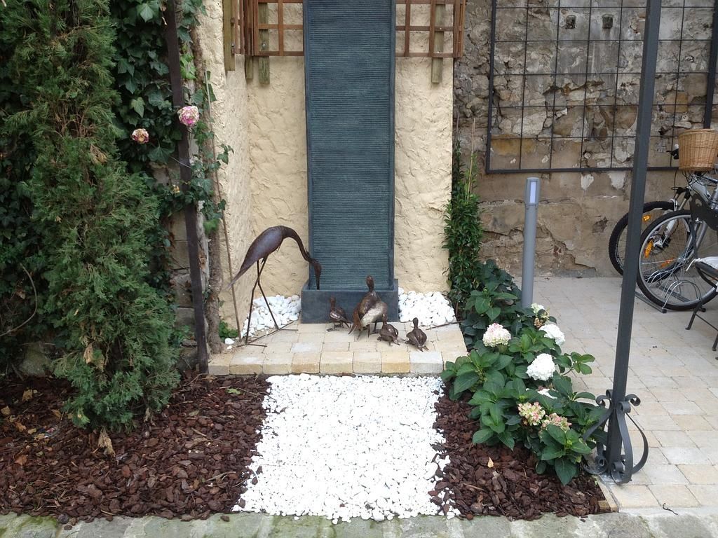 Une fontaine ornée de plantes décoratives et d'une statue d'oiseau, ainsi que des canards sur un chemin de pierre.
