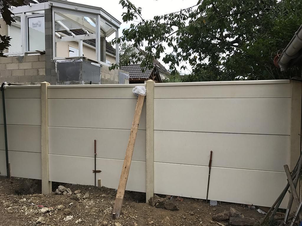 Clôture couleur crème avec poteaux en béton en construction.