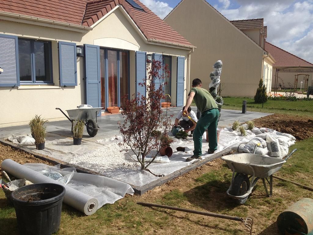 Des paysagistes installent des plantes et du gravier dans une terrasse de jardin résidentielle.
