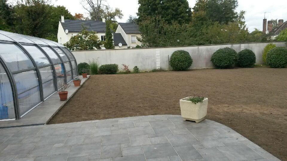 Jardin avec piscine sous dôme, terrasse et pelouse. Arbres et mur blanc en arrière-plan.