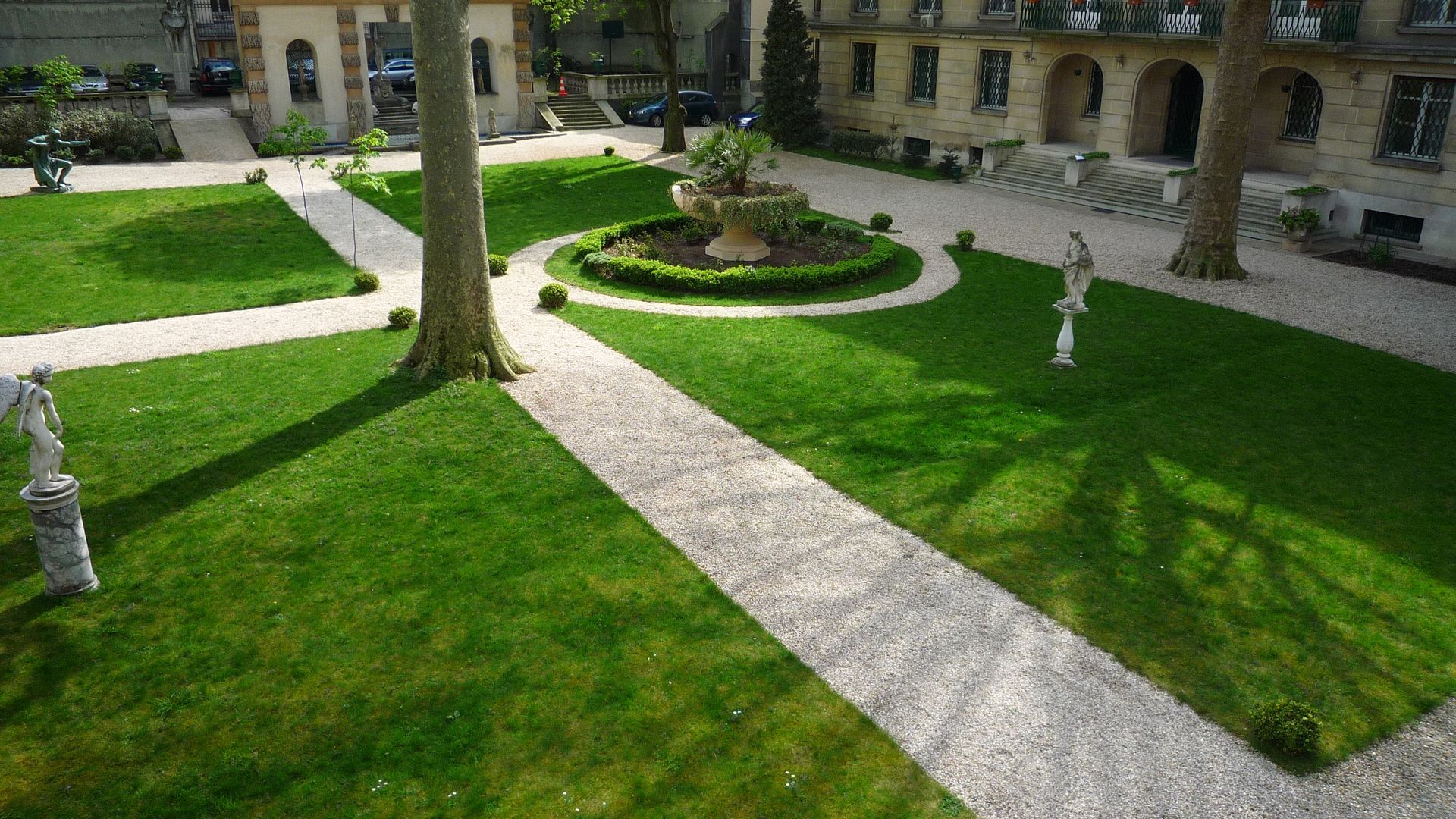 Espace vert avec statues et allée de jardin avec graviers
