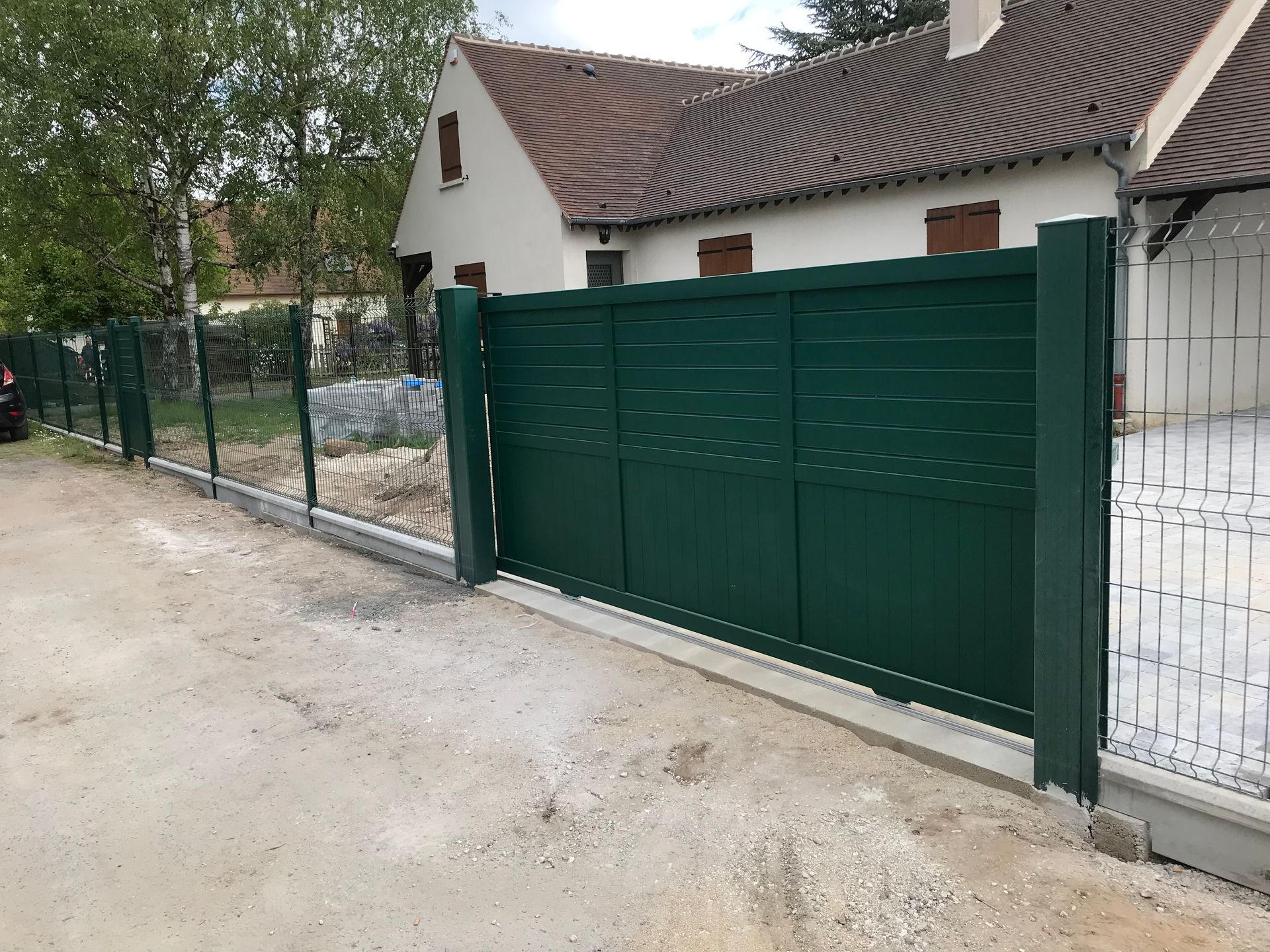 Portail coulissant vert devant une maison, installé sur une base en béton. Allée gravillonnée.