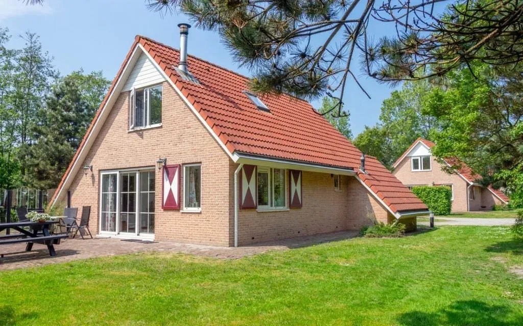 Een bakstenen huis met een rood dak en een picknicktafel ervoor.