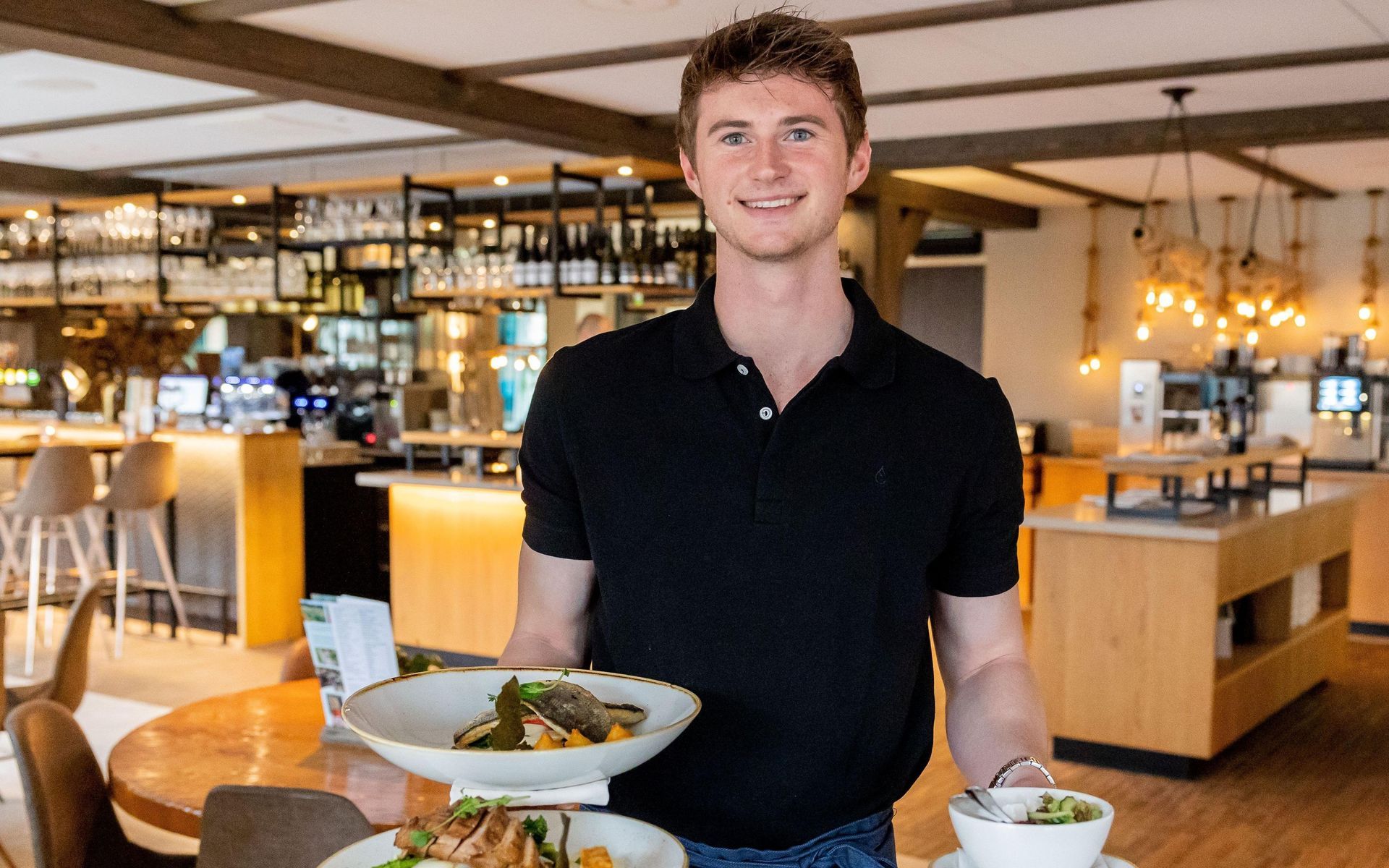 A man is holding two plates of food in a restaurant.